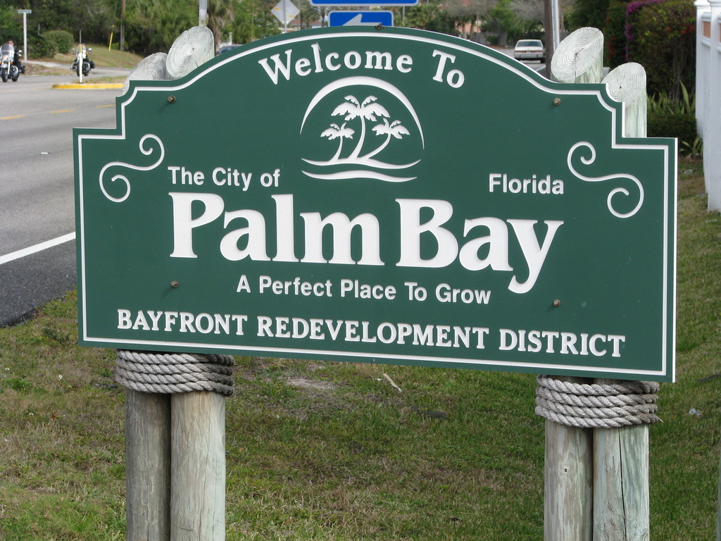 The green 'Welcome to The City of Palm Bay, Florida' sign on wooden posts.