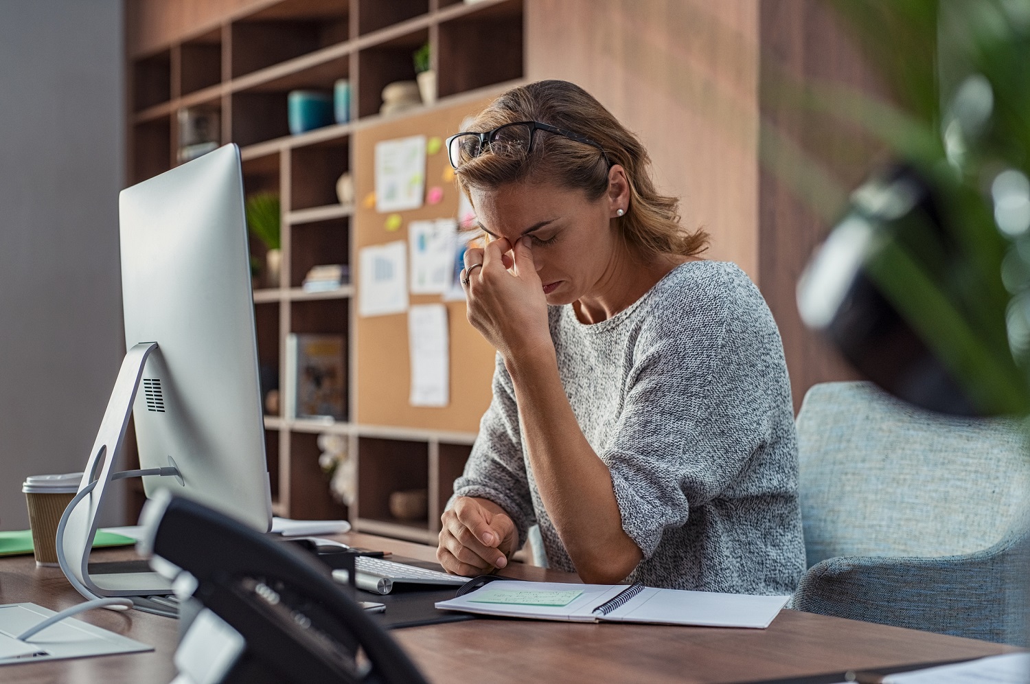 A stressed business owner at her desk, rubbing her eyes in front of a computer and notebook.